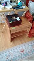 Photo showing the dark wooden men's jewellery box placed on top of the light pine small table, both visible with other household items around.