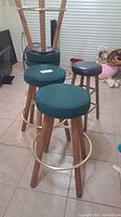 Set of five bar stools arranged on tile floor: 4 green fabric swivel stools and 1 shorter black vinyl stool.