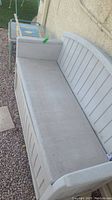 Photo showing the Suncast weathered storage bench with a slatted back, dusty and dirty surface, placed on gravel.