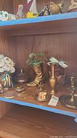 Shelf with brass cowboy boots, cowboy hat, vases, candle holders, small lidded container, and decorative bell