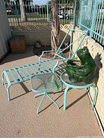 Light blue painted metal chaise lounge frame, frog planter sitting on one of the tables, smaller table with square glass top visible
