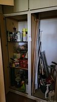 Image of storage cabinet shelves filled with assorted cleaning chemicals, oil container, painting tools including paint rollers and squeegees