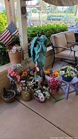 Wide view of patio area showing angel statue, small blue stool, numerous faux floral arrangements in various planters, American flag, and seating area