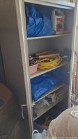 Metal cabinet shelves with blue tarps, extension cord, and wooden-handled gardening tools