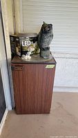 Full view of mini refrigerator with woodgrain finish, topped with boxed LED string lights, garden owl figurine, and dog figurine.