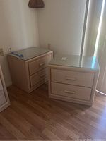 Front and angle view of two matching light wood nightstands with glass tops and two drawers each, showing their size and condition.