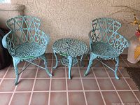 Full set of two wrought iron chairs and one matching round bistro table displayed on tiled floor near stucco wall
