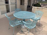 Photo showing round wrought iron outdoor table and four matching wrought iron chairs on a patio, all painted light blue.