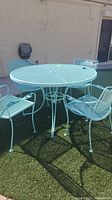 Front view of round painted wrought iron mesh table with four matching chairs arranged around it on artificial grass.