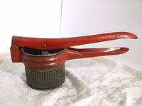 Side view of the metal potato masher ricer showing red painted long handles and perforated metal strainer section.