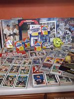 Photo showing a variety of baseball cards laid out including unopened packs of Fleer, Starting Lineup, and Chipz, mixed loose cards, and Topps Stadium Club framed photos, plus the Brockton Rox souvenir program and other memorabilia.