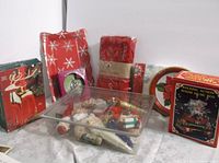 Lot contents including boxed rocking action wood music box, gold reindeer candle holder, wrapped plates and napkins, and clear container of vintage ornaments.