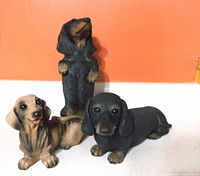 Three dachshund figures on light surface with orange wall background, showing different postures including standing and lying figures.