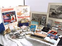 Photo showing the full arrangement of assorted vintage collectibles including advertisements, razor sets, needle book and box items on a white cloth.