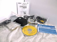 Nikon Coolpix 5900 digital camera, cables, software CD, carrying case, and manuals packed for the lot, all items shown on a white surface.
