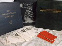 Three stamp albums and a pile of postal covers and booklets arranged on a cloth surface.