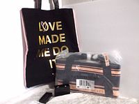 Black tote bag with gold lettering and pink sides plus striped tote bag sealed in plastic with tags.