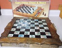 Full view of the hand-carved wooden chess board with checkered illustrated squares showing fairies and flowers, with original box in background illustrating chess set.