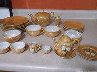 Overview of entire 18-piece tea set with teapot, cups, plates, and mini set pieces arranged on counter.