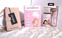 Photo showing Steve Madden pink crossbody wallet, Flawless Contour facial roller in package, and electric face cleansing brush in box.