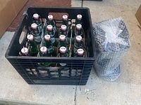 20 green Grolsch bottles with white and red hinged caps inside a black crate, with bubble wrap next to the crate