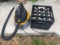 Stinger wet/dry vacuum with attached hose, black plastic crate filled with 20 green Grolsch beer bottles with flip-top caps, placed outside on ground.