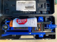 Open black plastic carrying case containing Duralast blue 3 ton hydraulic trolley jack with instruction manual.