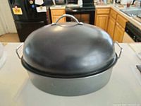 Photo of the closed black metal roaster with domed lid on a kitchen counter.