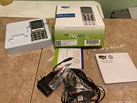 Flex MT Plus device with screen, buttons, original box, power adapters, manuals and cables on table.