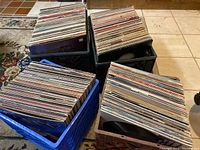 Four crates of vinyl LP albums in blue, black and white crates on floor