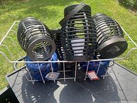 View of five black cage-style solar yard light lanterns arranged in a metal rack outdoors. Lantern tops show integrated solar panels with black metal slatted construction.