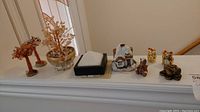 Shelf displaying a collection of miniature Asian decor items including gemstone trees, ceramic house, maneki-neko figurines, frog figurine, reindeer figurine, and fabric box.