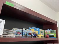 Top shelf with a collection of toy cars, trains, figurines, and greeting cards arranged in packaging and loose formats.