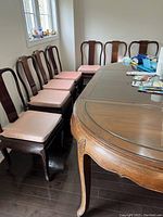 View of the rosewood dining table with glass top and several wooden chairs with pink cushions around it.