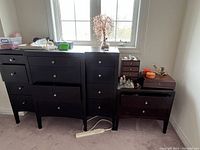 Front and partial side angle of dresser in room setting with some items on top and around.