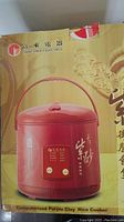 Box photo showing the red computerized purple clay rice cooker with traditional Asian script and brand name 'Grant Profit Electrics'.
