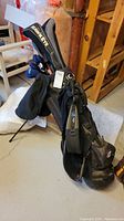 Photo of black Callaway golf bag with Hawkeye club head covers, shoulder straps, and stand visible against basement environment.