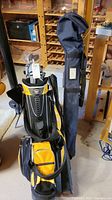 Golf bag containing golf clubs standing next to a navy blue carrying case, placed in a basement storage area with wooden shelving in the background.