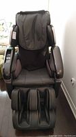 Front view of black synthetic leather massage chair showing seat, armrests, foot and calf massager, control panel