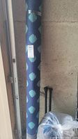 Rolled blue outdoor rug leaning against wall showing large polka dot design and label.