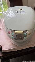 Front view of white Galanz rice cooker showing control panel with pastel colored function buttons and digital display