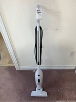 Front full view of vacuum showing upright white vacuum and cord wrapped around the handle with auction tag attached.