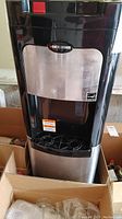 Front view of Black & Decker bottom feed hot and cold water dispenser showing black and stainless steel front panel with logo and dispensing area with drip trays.