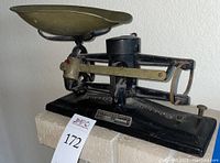 Side view of The Torsion Balance Co. balance scale showing black metal base and brass pan