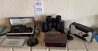 Full lot arranged on surface including camera, binoculars, clock, radio, tape, and mystery object