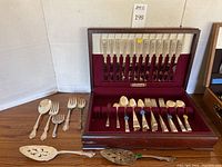 Full view of the wooden display case with Community silverplate flatware and additional serving utensils arranged in front of the case on table.