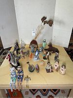 Wide angle shot of entire lot showing various ceramic, porcelain, wooden, plastic figurines and decor pieces arranged on yellow tablecloth.