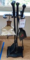 Complete fireplace tool set displayed on iron stand, showing poker, tongs, shovel, scoop with painted cherries, and leather bellows.