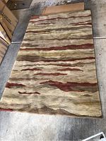 Full view of the Ano Zeno hand knotted wool rug laid flat on concrete floor showing the abstract horizontal stripe pattern in beige, olive green, rust red, and tan colors.