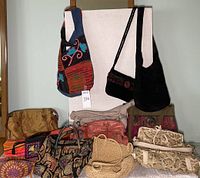 Full lot showing 13 assorted hand and shoulder bags consisting of various fabrics, patterns, and styles arranged in front of a white board.
